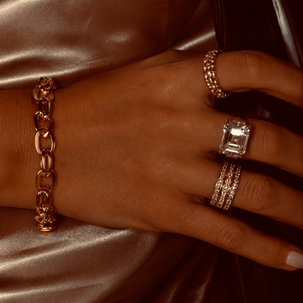 Close-up of a hand wearing a GLORIASAA gold chain bracelet and stacked rings